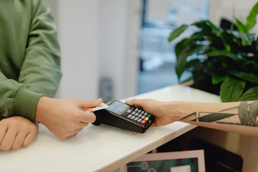 A hand tapping a bank card on a payment terminal at a shop counter